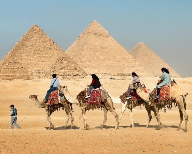Four People Riding on Camels Across the Pyramids