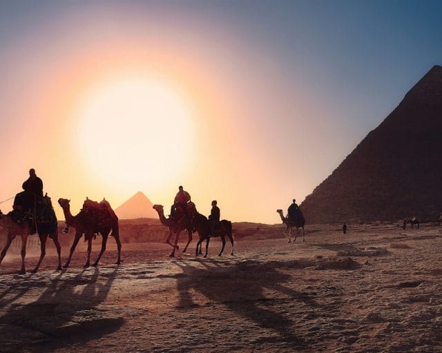 five persons riding camels walking on sand beside Pyramid of Egypt