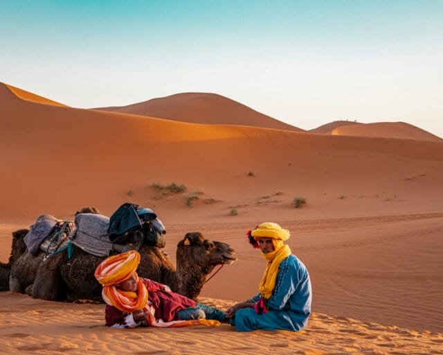 man in yellow robe sitting on brown sand during daytime